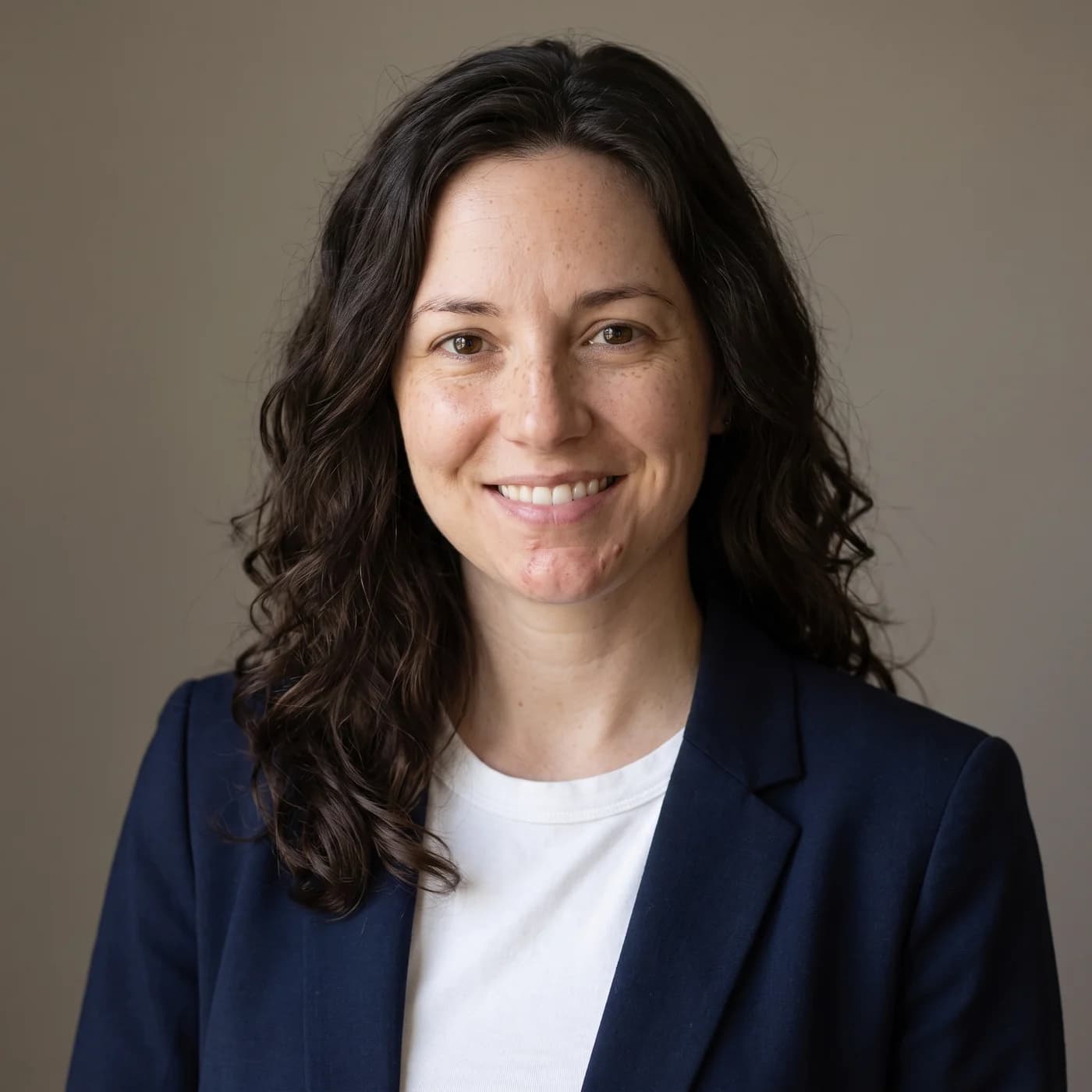 A studio headshot of the woman from the selfies, in a navy blazer against a grey backdrop.